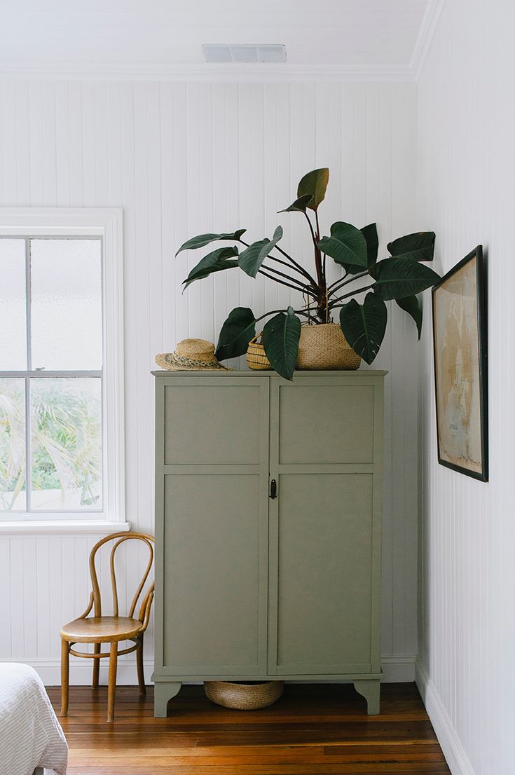 a green cabinet sitting in the corner of a room next to a chair and potted plant