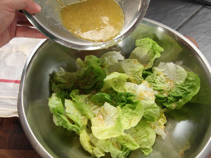 lettuce in a bowl being stirred with a strainer by someone's hand