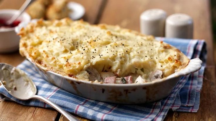 a casserole dish with meat and cheese in it on a wooden table next to two spoons