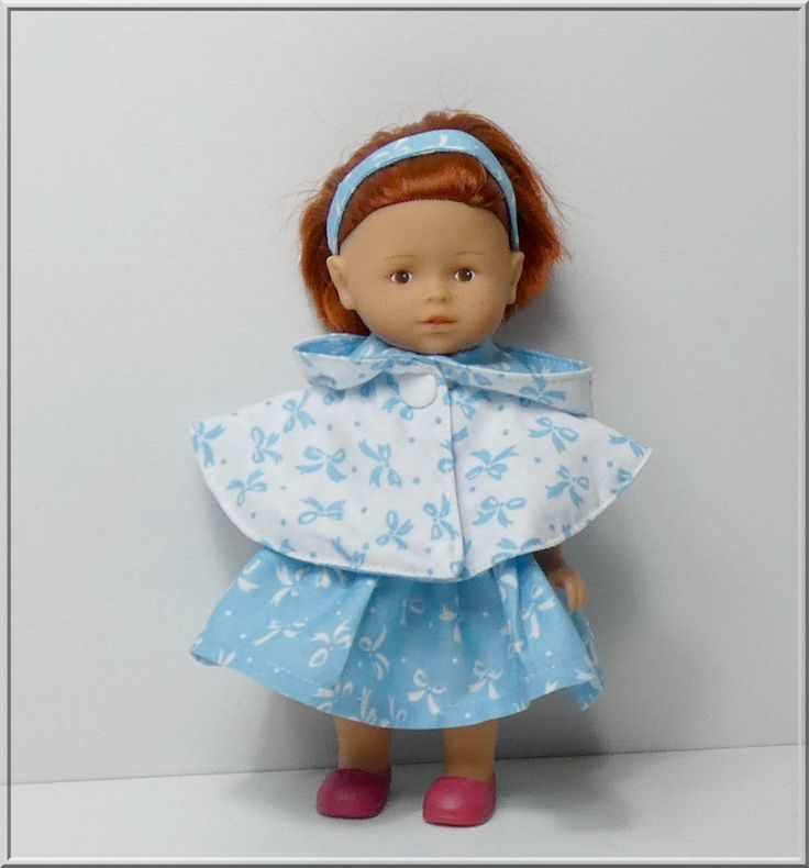 a doll with red hair wearing a blue dress and pink shoes, standing against a white wall