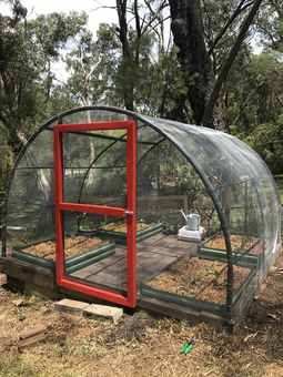 a red and green chicken coop in the middle of a field with dirt on the ground