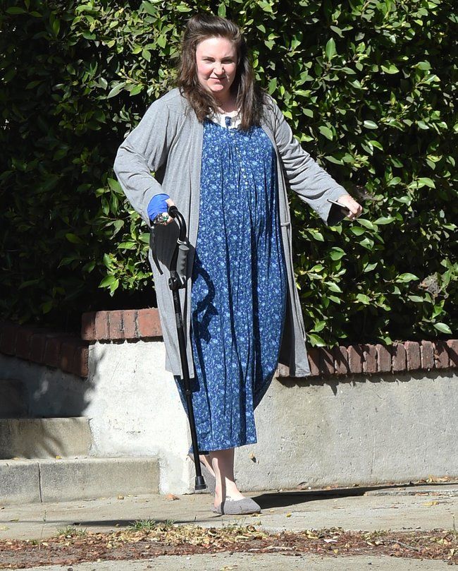 a woman in a blue dress is walking with an umbrella on the sidewalk near some bushes