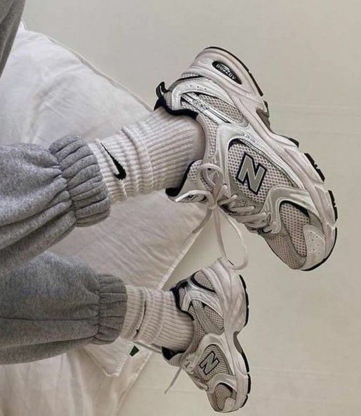 someone in grey and white sneakers is holding their feet up against the wall with one hand