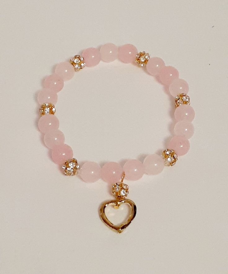 Rose quartz is known as the stone of love and reconcilliation and is customarily used as a gift of love.   It is thought to make one open to love and compassion.  Some believe that rose quartz has calming effects and helps to develope strong friendships. Two styles of bracelets are shown : # 1 - 8mm genuine rose quartz beads  with silver & rhinestone accent bands and an open silver heart charm.  #2- 8 mm genuine rose quartz beads with rose gold & rhinestone accent clusters and an open rose gold heart charm. Rose quartz is typically a cloudy translucent pink colour.  These bracelets are sure to plesse with its delicate colour of pink and silver or gold accents. This stretch rose quartz bracelet is made with natural pink rose quartz stones that have been polished to a glossy finish. It featu Gold And Pink Bracelet, Pink And Gold Bracelet, Pink Natural Stones Jewelry For Friendship, Pink Heart-shaped Spiritual Beaded Bracelets, Elegant Rose Quartz Crystal Bracelet For Meditation, Pink Natural Stone Bracelets For Friendship, Pink Natural Stones Bracelet For Friendship, Spiritual Rose Quartz Jewelry For Friendship, Spiritual Pink Bracelet As Gift