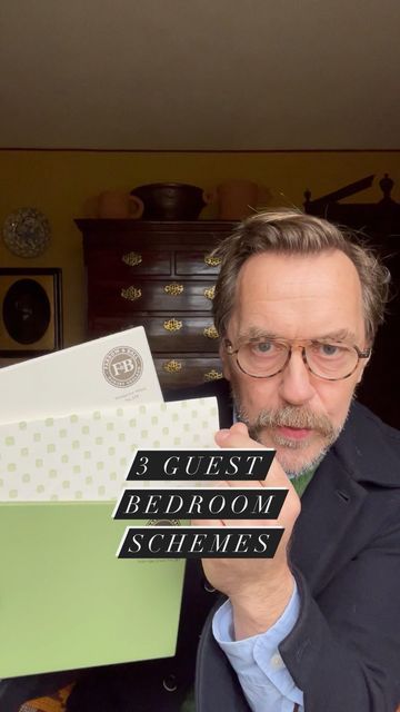 a man in glasses holding up a sign that says guest bedroom schlemes