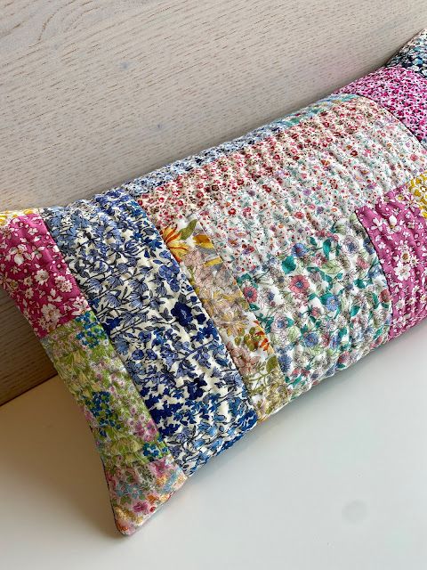 a multicolored patchwork pillow sitting on top of a white table next to a wooden headboard