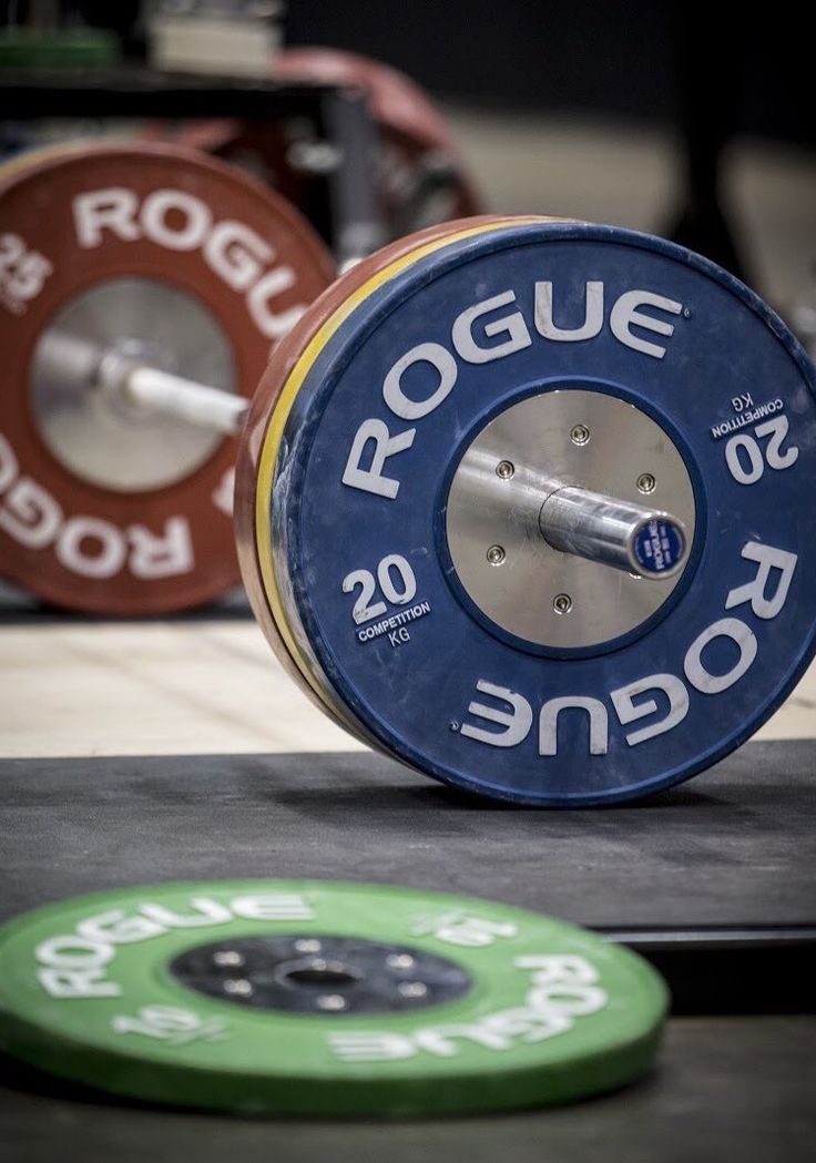 a barbell weight sitting on top of a gym floor next to a green disc