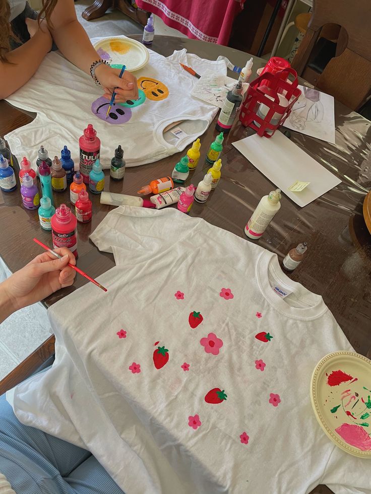 a woman sitting at a table making t - shirts with crayons on it