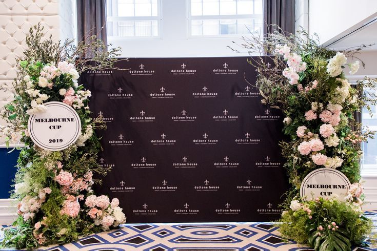 two floral archways are set up in front of a black backdrop with white and pink flowers