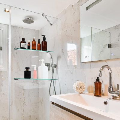 a bathroom with white marble walls and shelves filled with soap, lotion, and hand sanitizers