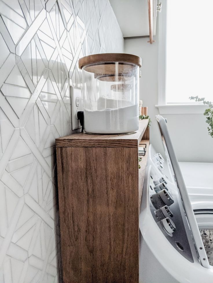 a white washer sitting next to a wooden cabinet in a room with geometric tiles on the wall