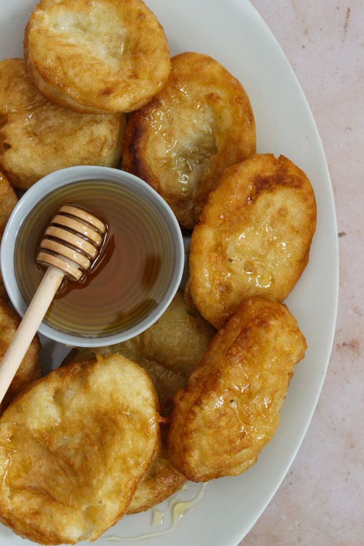 some fried food on a white plate with a honey dip in the middle and a wooden spoon