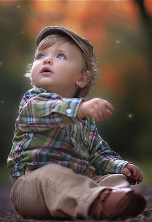 a little boy sitting on the ground with his hands out and looking up at something