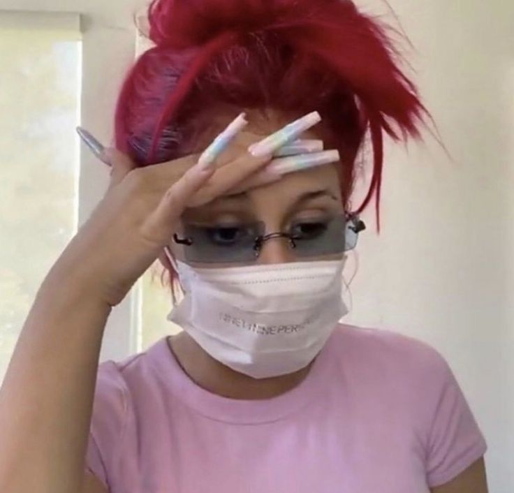 a woman with red hair wearing a face mask and holding her hands to her head