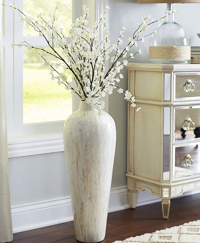 a white vase with flowers in it sitting next to a dresser and window sill