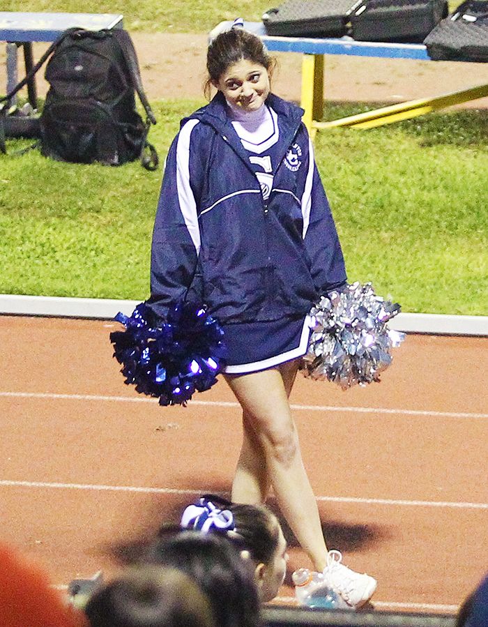 a cheerleader walking on the sidelines with her pom poms