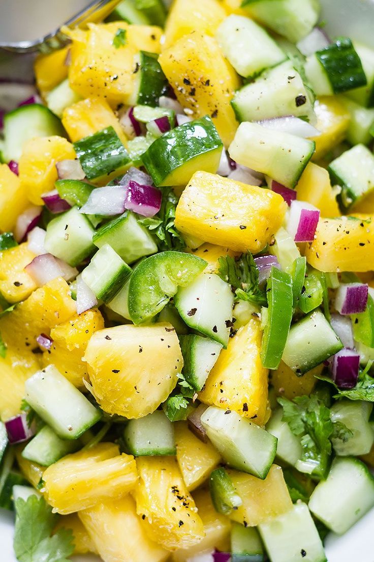 a white bowl filled with cucumber, pineapple, and other veggies