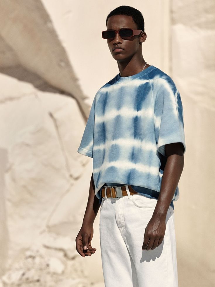 a young man wearing sunglasses and a tie - dyed shirt stands in front of a rock formation