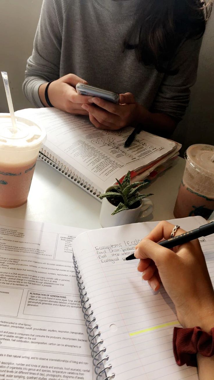 a person sitting at a table with notebooks and a cell phone in front of them