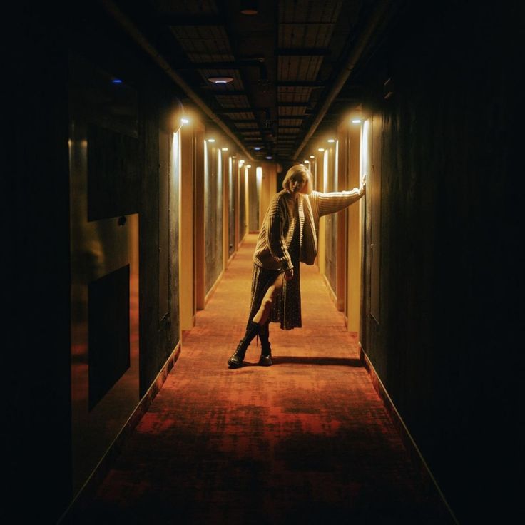 a woman is standing in the middle of an empty hallway with her arms outstretched and legs crossed