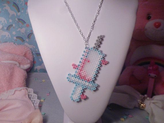 a cross stitch necklace on a mannequin next to a teddy bear and other items