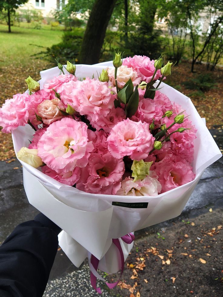 a person holding a bouquet of pink flowers in their hand on the sidewalk near some trees