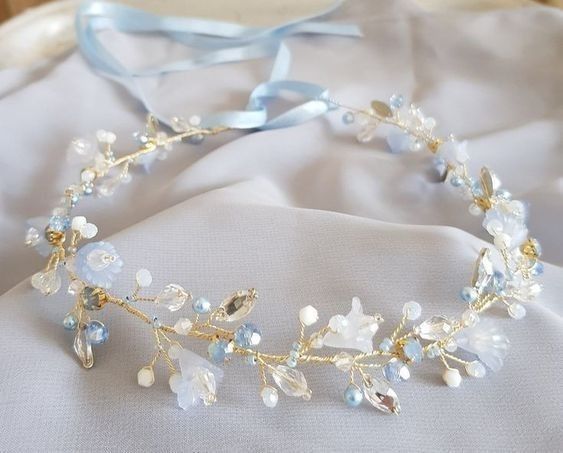 a tiara with blue and white flowers is laying on a bed next to a light blue ribbon