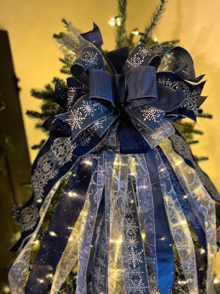 a blue and white christmas tree decorated with snowflakes, ribbons and lights in front of a yellow wall