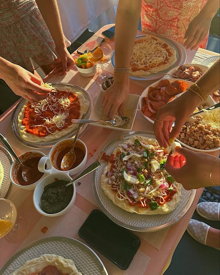 several people are making pizzas at a table with other food items on the table