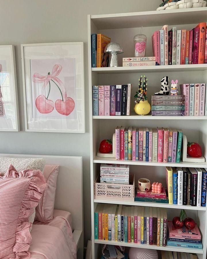 a book shelf filled with lots of books next to a neatly made bed covered in pink and white sheets