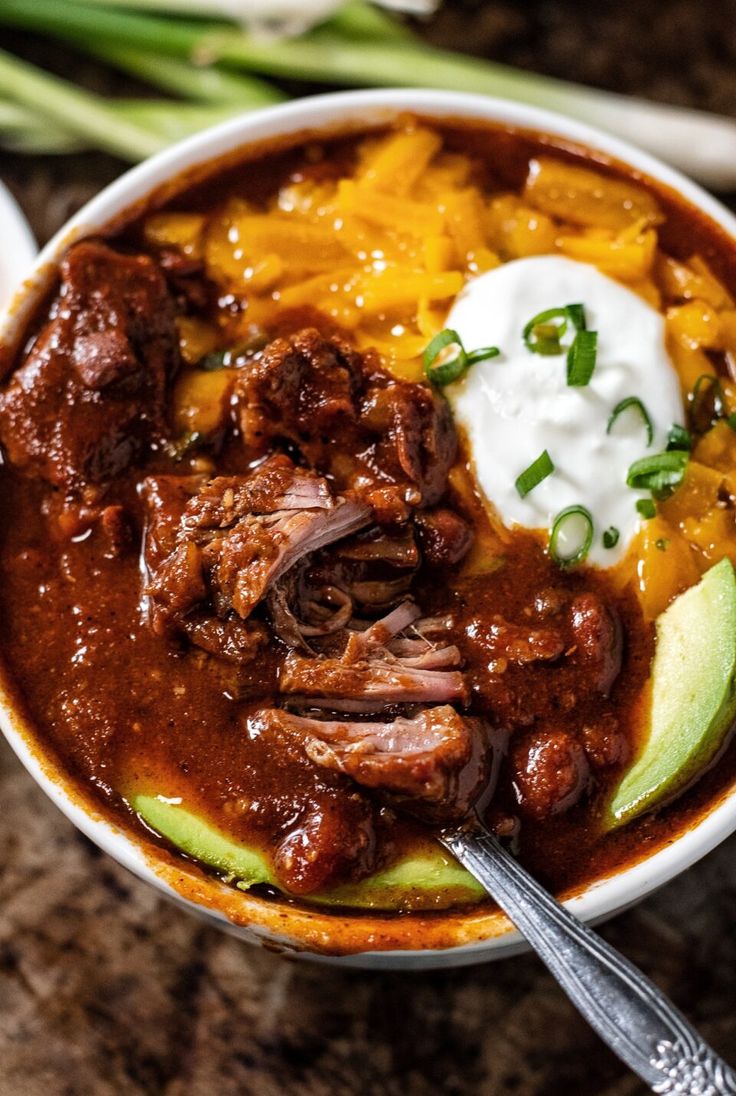 a close up of a bowl of food with meat and sour cream on the side