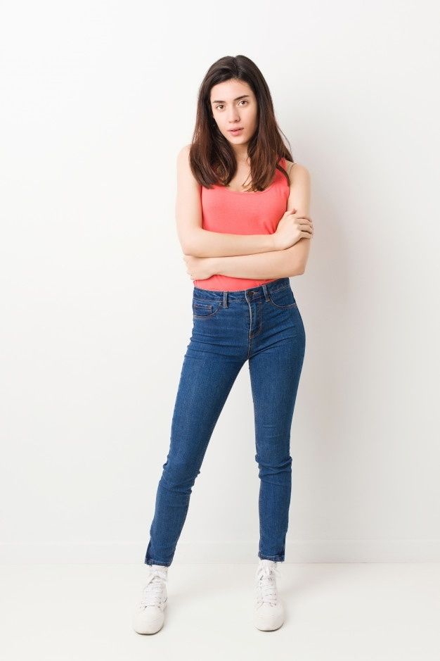 a woman standing with her arms crossed and looking at the camera while wearing high rise jeans