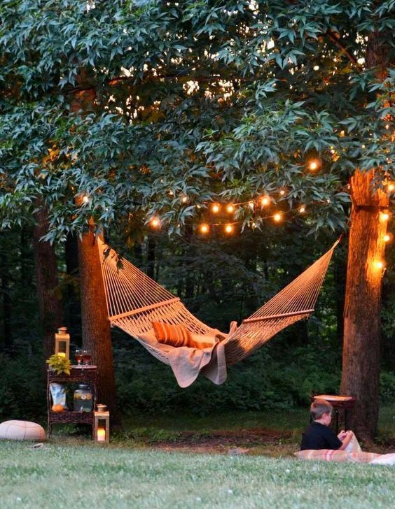 an image of a hammock in the woods with lights strung from trees and benches