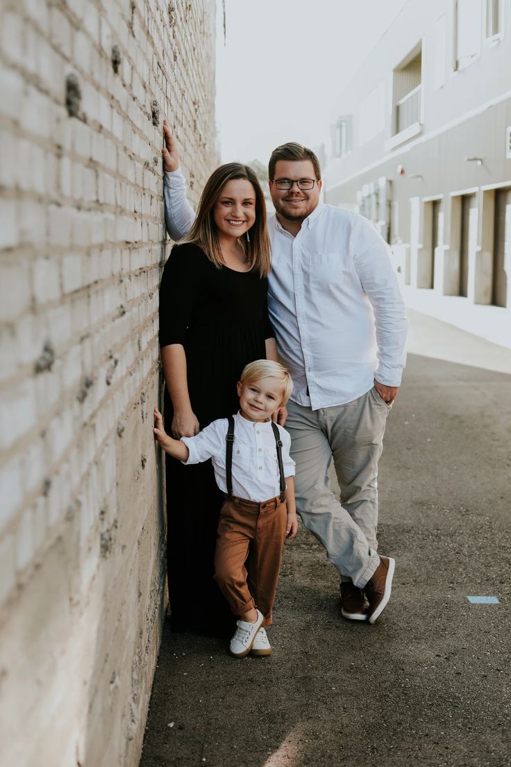 a man and woman standing next to a brick wall with a small child in front of them