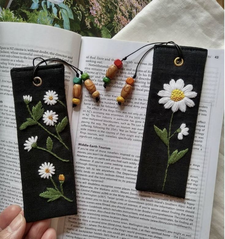 two bookmarks with daisies and leaves on them are hanging from the pages of an open book