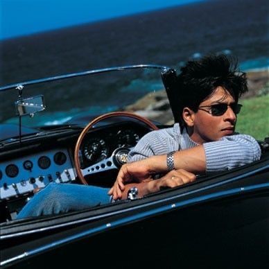 a man sitting in the driver's seat of an old fashioned sports car near the ocean