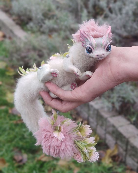 a person holding two small white and pink animals in their hands, with grass behind them