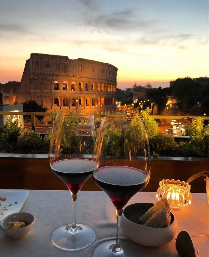 two glasses of wine are sitting on a table overlooking the roman colossion at sunset