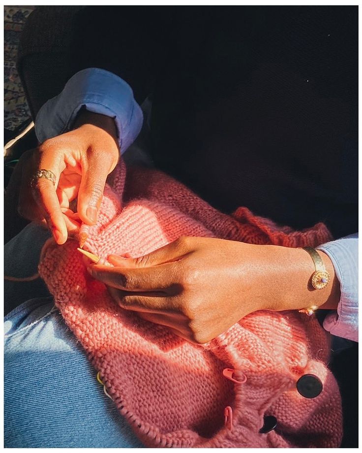 a woman is knitting on a pink blanket