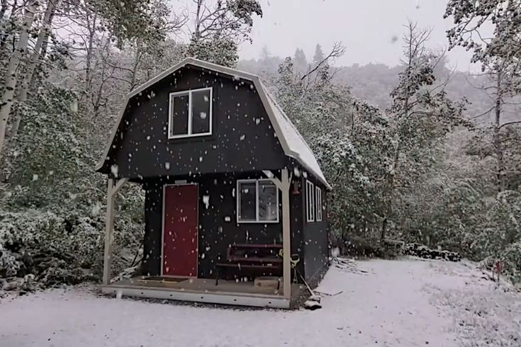 a small black cabin in the woods covered in snow