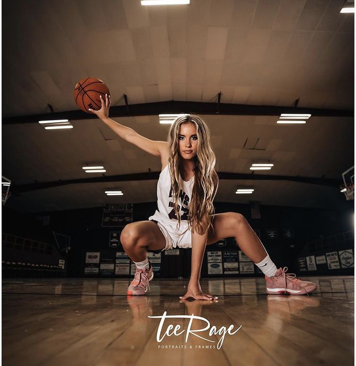 a beautiful young woman holding a basketball on top of a hard wood floor