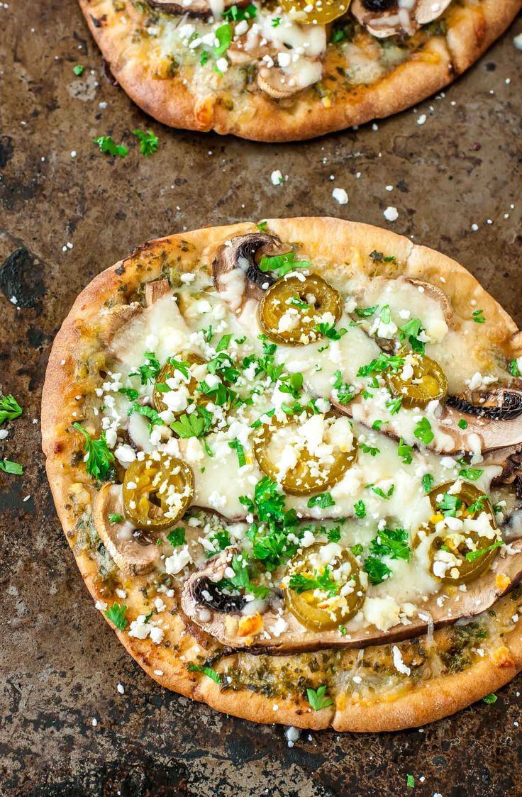 two pizzas with mushrooms, cheese and parsley on them sitting on a table