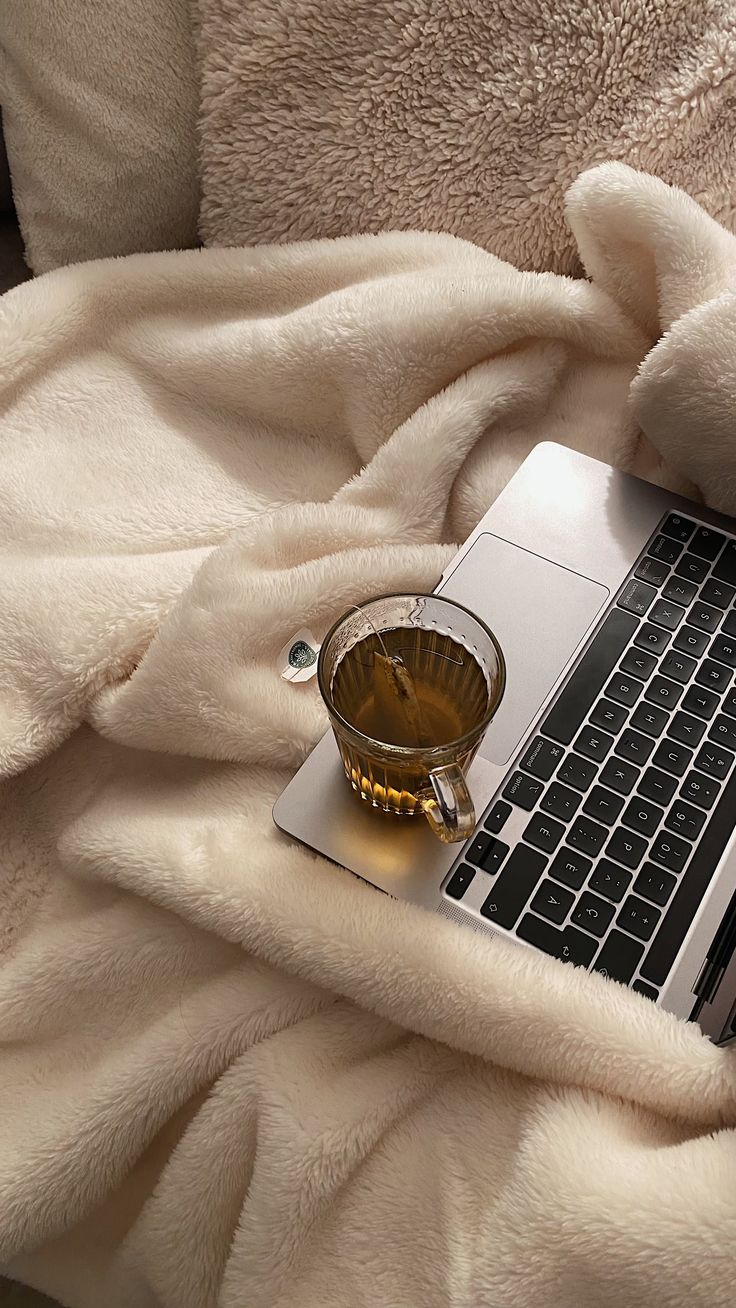 an open laptop computer sitting on top of a bed next to a cup of coffee