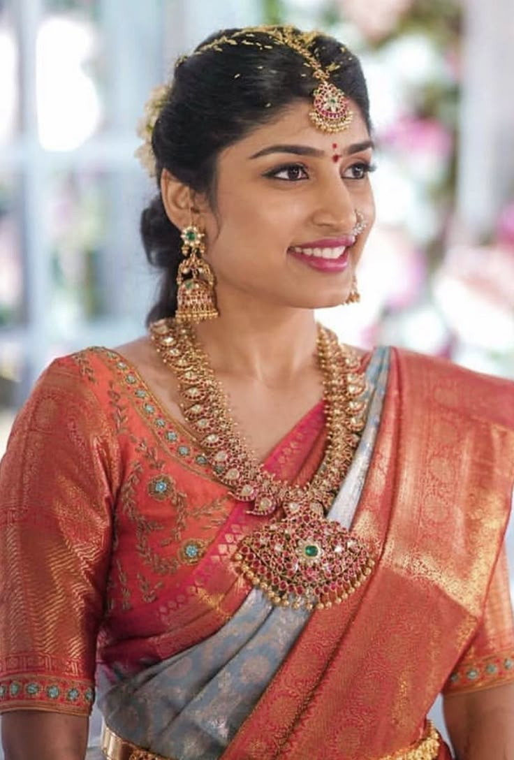 a woman in an orange and grey sari with gold jewelry on her neck, smiling