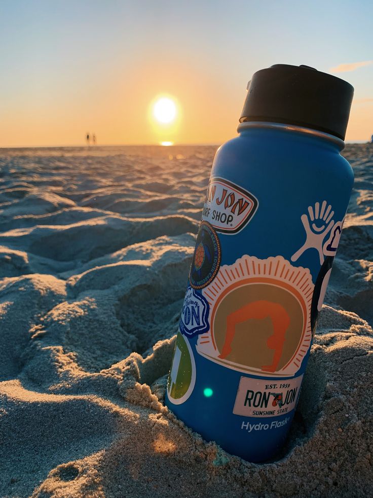 a blue water bottle sitting on top of a sandy beach