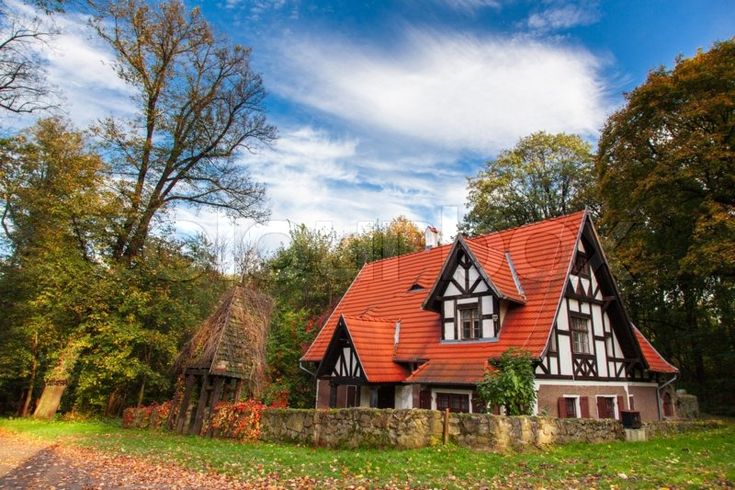 an old style house with red roof and white trim on the front, surrounded by trees