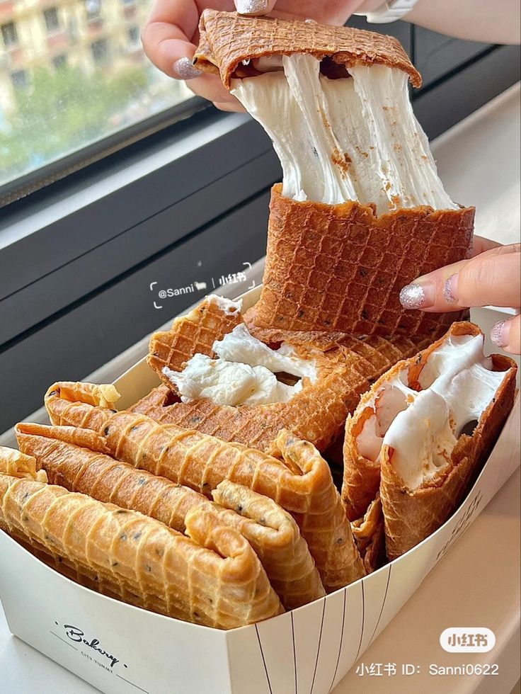 a person is eating waffles and ice cream in a box on a window sill