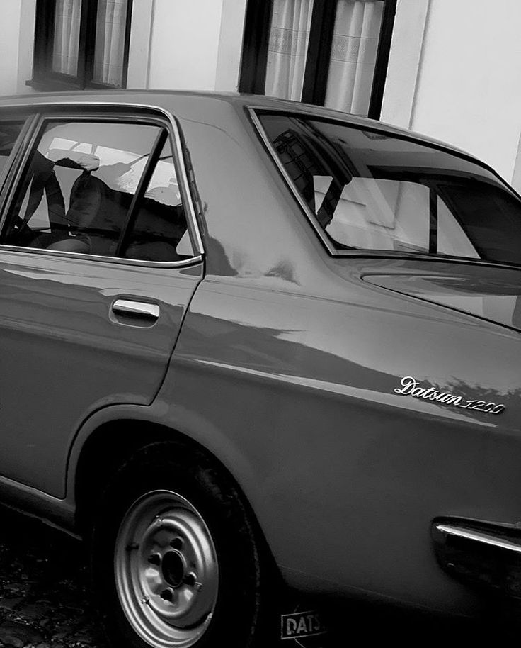 a black and white photo of a car parked in front of a building with the door open