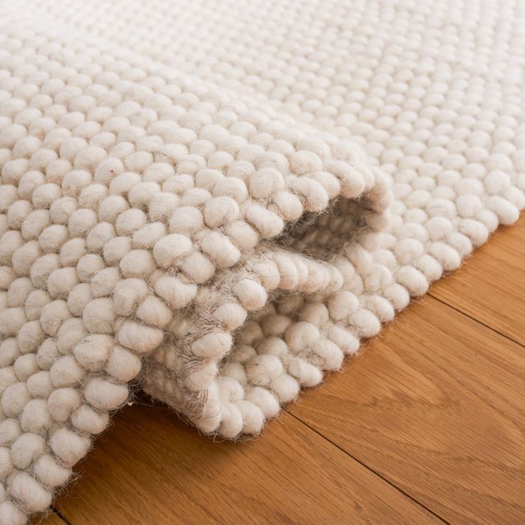 a close up of a rug on the floor with wood floors and white wool balls