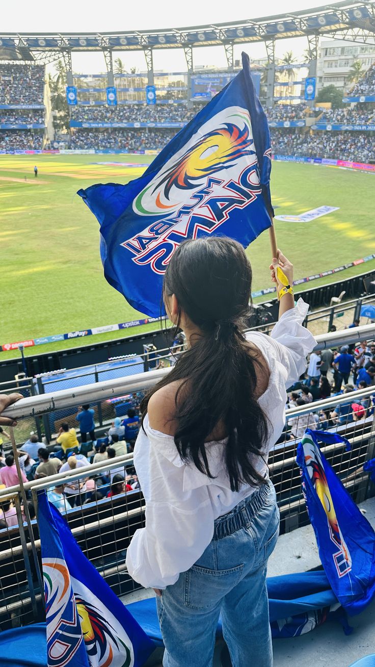 a woman holding a blue flag in front of a crowd at a baseball game on a sunny day